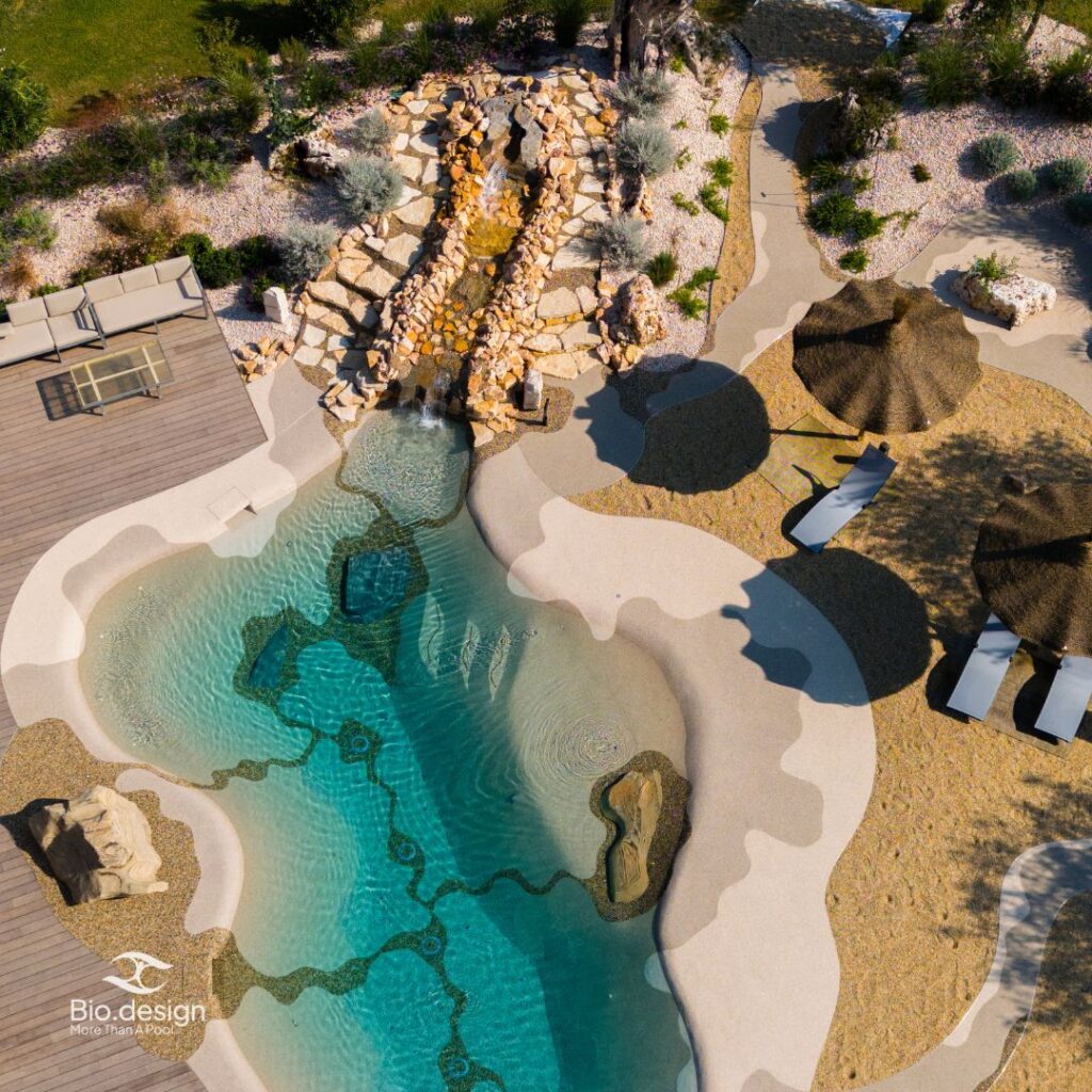 Biodesign Pool mit Wasserfall aus Naturstein und Holzdeck