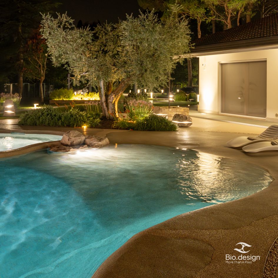 Beleuchteter Biodesign Pool am Abend mit Olivenbaum
